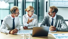Gruppe von Sachverständigen im intensiven Fachgespräch an einem Besprechungstisch mit Unterlagen und Laptop